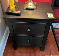 Front view of black two-drawer nightstand with lamp and phone on top