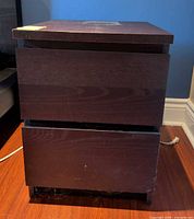Front view of dark brown two-drawer side table showing closed drawers and veneer chips at base