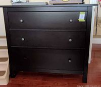 Front view of black-brown three-drawer dresser showing overall appearance and missing knob on bottom drawer