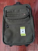 Front view of olive green American Tourister carry-on with front pocket and logo badge visible