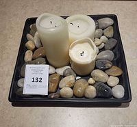 Top view of three cream pillar candles on black tray with multicolour stones