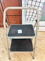 Front view of beige metal 2-step ladder showing both steps and frame