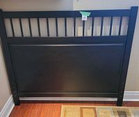 Full view of black headboard against wall, shows slat design and panel