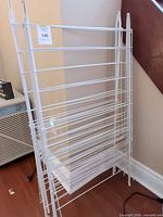 Front view of two white metal folding laundry drying racks leaning against wall