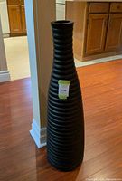 Full view of tall black ribbed vase on floor