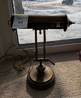 Full view of brass desk lamp showing shape and window backdrop