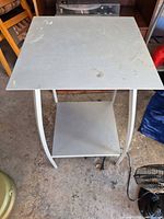 Light grey steel square table with lower shelf; shows condition and design