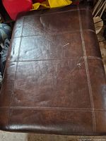 Top view of brown vinyl footstool showing stitching pattern and surface wear