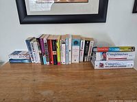 Single overview image of all books lined on tabletop; paperbacks upright center, two books stacked left, four cookbooks stacked right