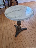 Full view of round marble-top side table showing marble surface, wooden column and metal tripod base