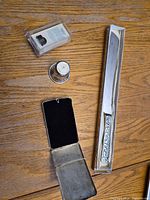 All five items arranged: boxed thimble, sterling cup, open cigarette case, plated cutter