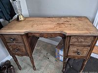 Front view of wooden desk showing drawers, turned legs and surface wear; glass lamp on top