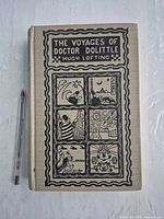 Front cover of cloth hardcover with detailed black illustration, pen for scale