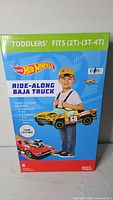Front of sealed retail box showing Hot Wheels Ride-Along Baja Truck toddler costume, size range 2T-4T