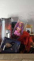 Overall lot view showing Barbie, Spike figure, lightsaber, Star Wars box, red plush hair and dinosaur