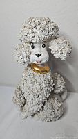 Front view of white ceramic poodle figurine with textured coat and gold collar