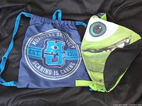 Both bags laid flat: navy drawstring backpack and Mike Wazowski face bag