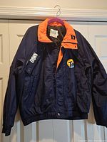 Front view of navy and orange Tide Racing jacket hanging