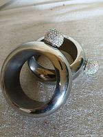 Two circular silver-tone bracelet flasks stacked, jeweled caps visible