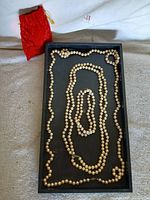 Tray displaying three pearl strands and red pouch