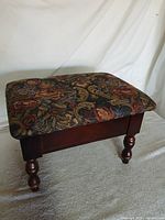 Oblique view of footstool showing cherry wood frame, turned legs, and floral tapestry top