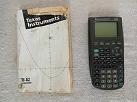 Front view of TI-82 calculator beside worn guidebook