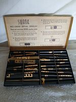 Open case showing compartments of gold-tone initials and instruction graphic