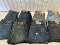 Eight folded pairs of jeans laid out showing back pockets and patches