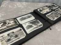 Album opened showing black pages with black-and-white photographs of houses and vintage car