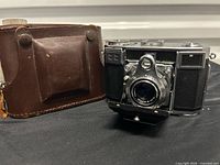 Camera front view with lens extended beside leather case