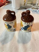 Front view of both jug-shaped shakers showing graphics and lettering