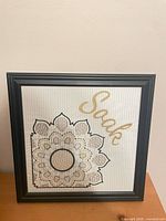 Front view showing framed cross stitch design and word “Soak”