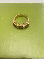 Top view of gold-tone ring showing three red rectangular stones in channel setting on green background