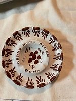 Top view of white ceramic ashtray showing Grand Hotel Flora Roma text and brown decoration