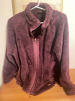 Front view of burgundy fleece jacket on hanger showing overall style and condition