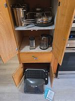 Open cabinet showing Lagostina pots and pans, grater, kettle, grill