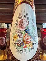 Close view of decanter medallion showing floral painting and gold trim, partial view of matching glasses