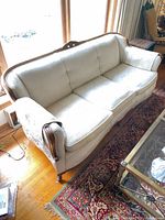 Front angle view of cream three-seat sofa showing upholstery, carved wood trim, seat cushions and legs