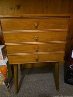 Front view showing four drawers with brass knobs and tapered legs