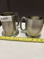 Front view of both pewter steins with tape for scale