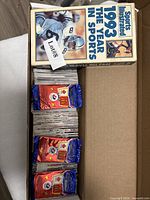 Box holding VHS tape and stacks of sports cards with sealed McDonald's coin packs visible
