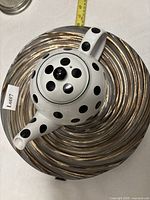 White ceramic polka dot teapot on gold swirl bowl with tape measure