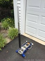 Full view of the floor jack on driveway showing blue aluminum frame, handle, and wheels