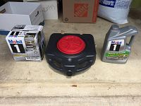 Photo showing eleven quarts of Mobil 1 0W-20 synthetic oil in original containers with two separate packs and a single container visible, alongside a black plastic Drainmaster oil pan with red lid.