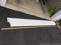 Four wood trim boards laid out on concrete and carpeted floor surface, including three larger white painted boards and one narrow unpainted board