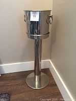Stainless steel ice bucket on stand, showing the assembled appearance and proportional size against the wall and floor.