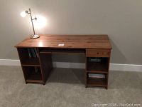 Desk shown from side angle with lamp on top, displaying open cubby shelves and smooth wood top surface.