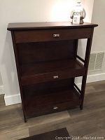 Front view of the dark wood bookcase showing three drawers and two open shelves with metal drawer handles.