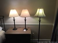 Overview of one floor lamp and two matching table lamps on and off a wooden chest of drawers against a beige wall