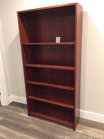 Front and angled front view of the tall cherry wood bookcase showing five shelves and reddish-brown finish. Visible scratches and wear on surfaces.